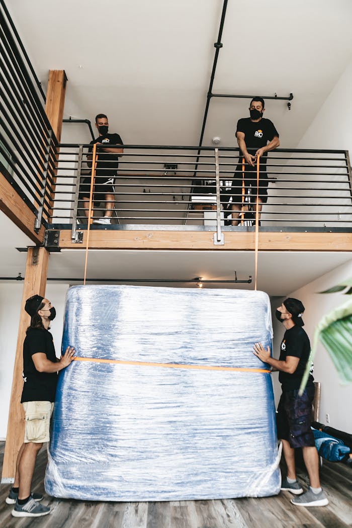 services-02 Four movers carefully lift a large wrapped object using straps indoors.
